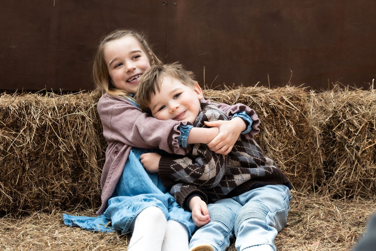 Children playing and laughing together while sitting on hay bales in a rustic barn setting.