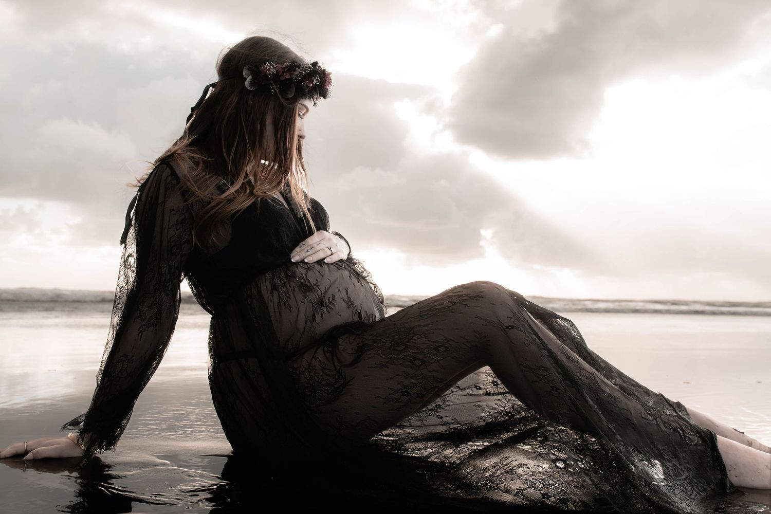 A person sits on a rocky beach at sunset with waves crashing in the background creating a moody silhouette.