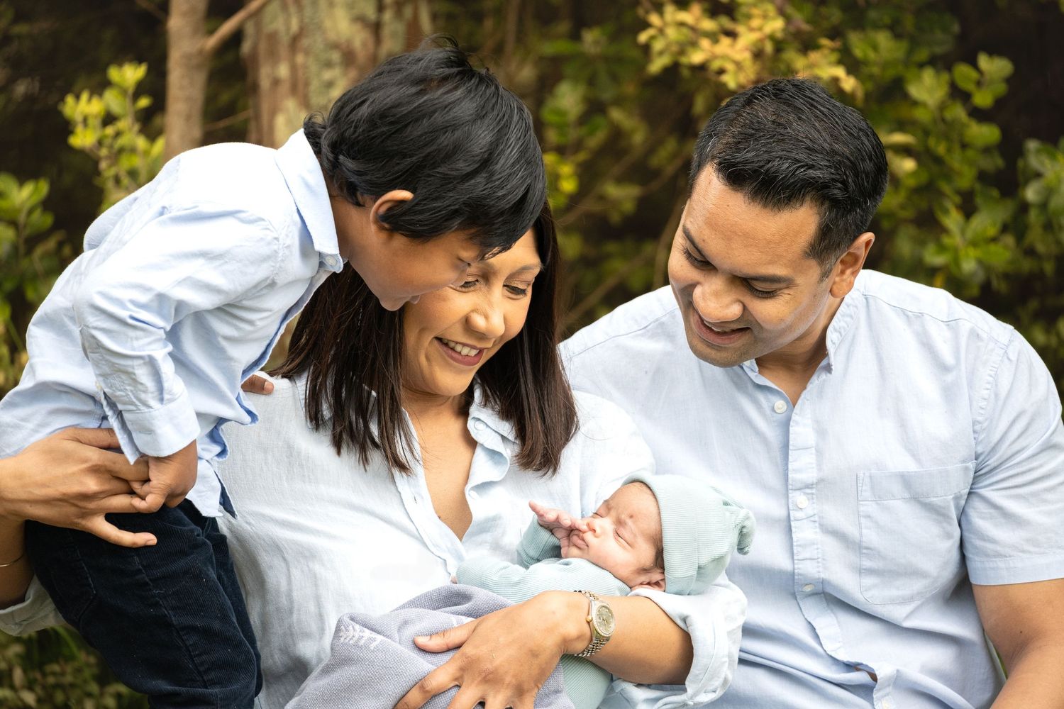 A family shares a joyful moment together while holding their newborn baby outdoors in a natural setting.