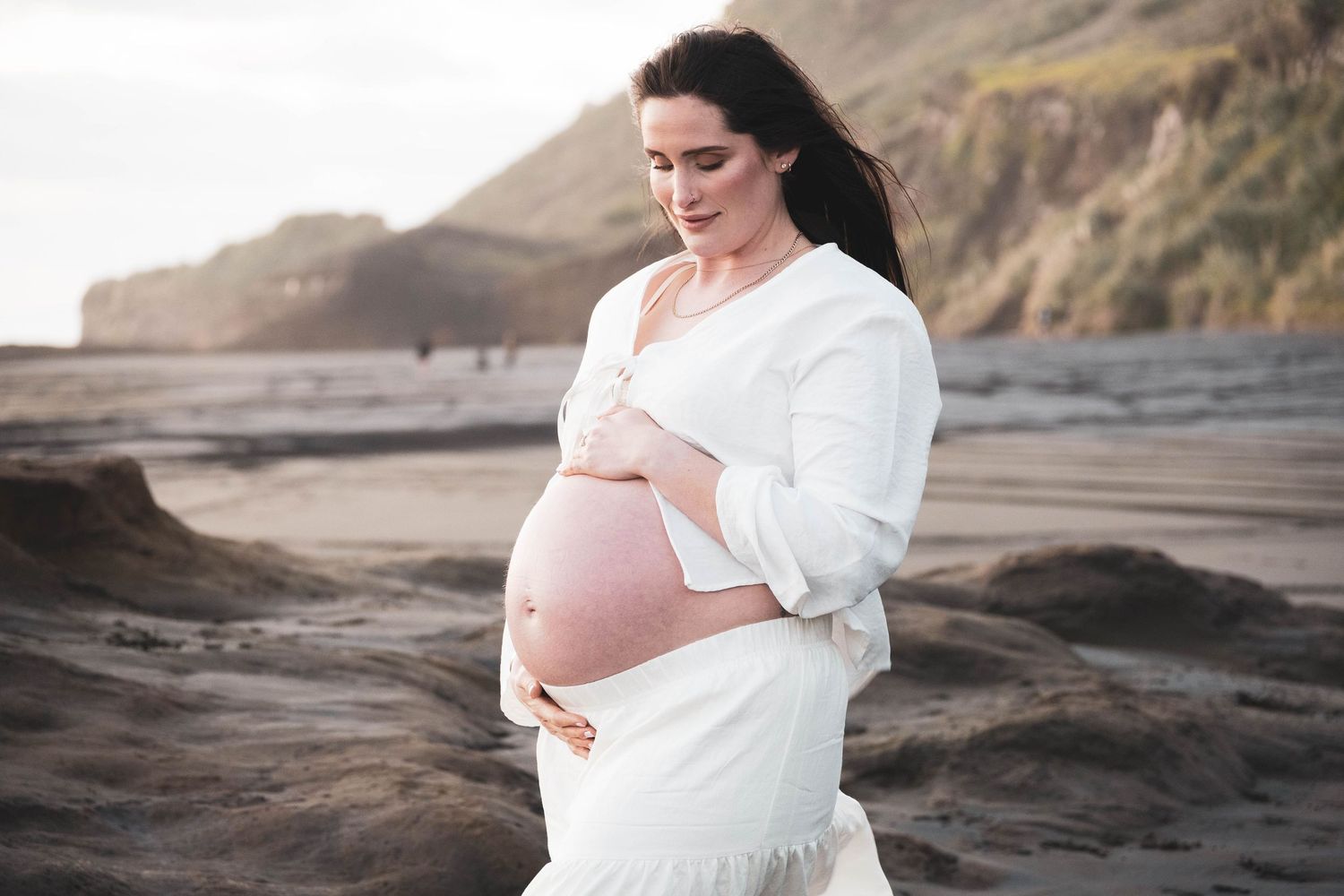 Maternity photos on rocky coastal cliffs with flowing white dress.