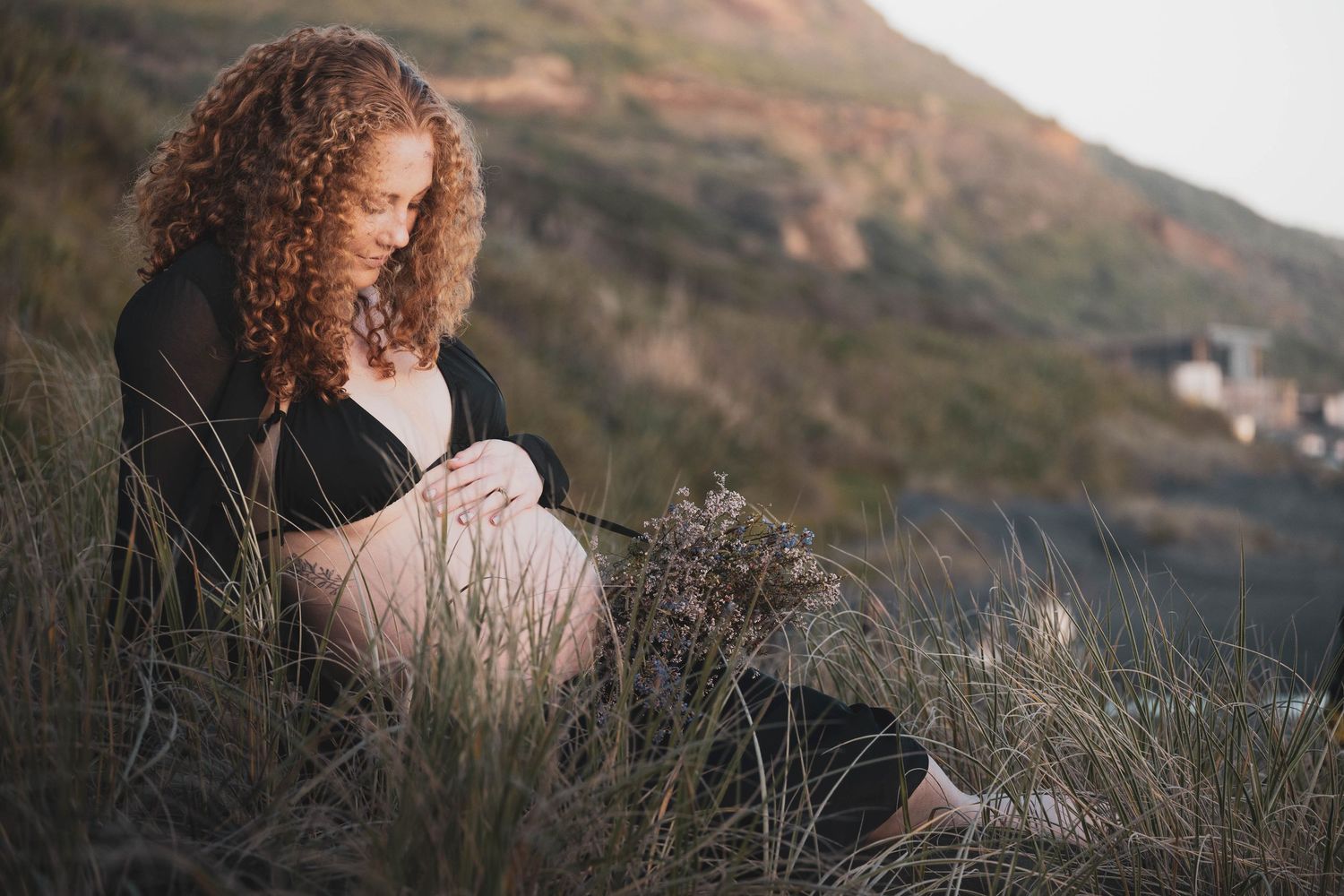 Scenic outdoor maternity photography session featuring grassy hillside at golden hour.