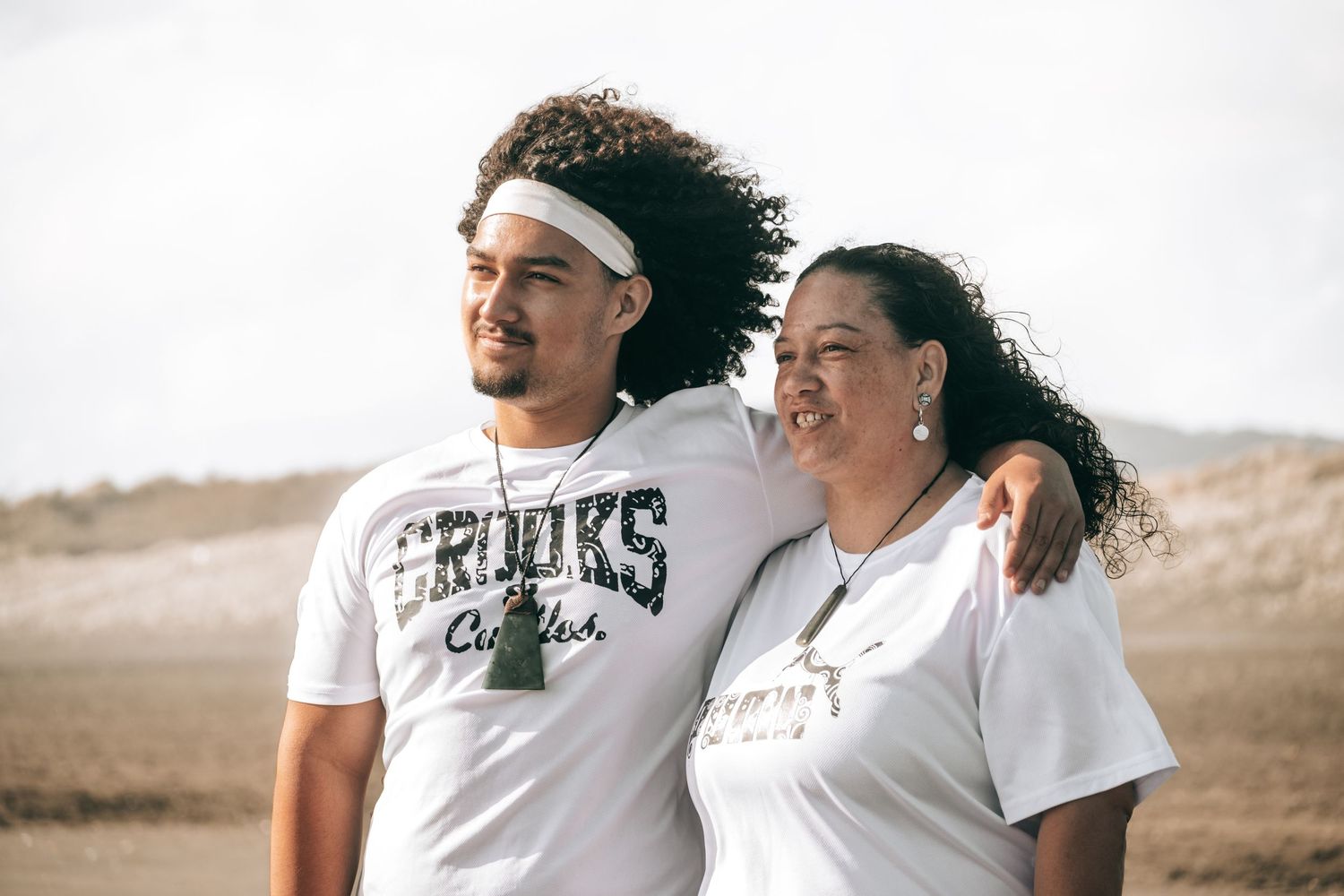Athletic couple in white t-shirts laugh and embrace while exercising outdoors in a desert landscape.