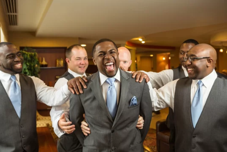 Groomsmen in blue ties and gray suits sharing laughs before wedding.