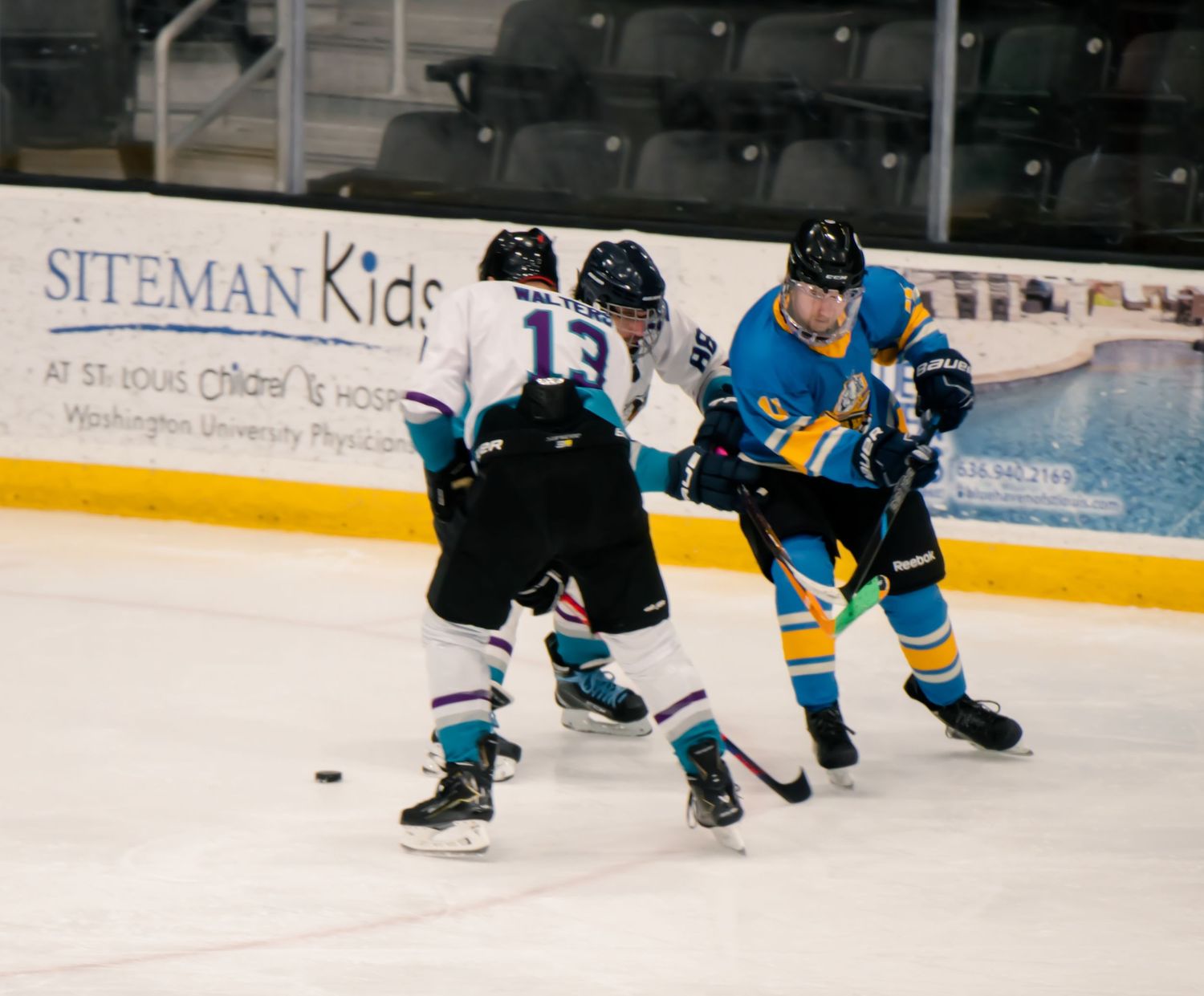 Hockey players in blue and black uniforms skate on ice during a competitive match.