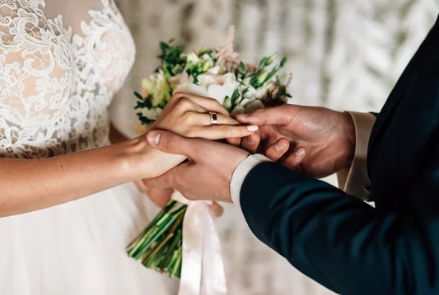 Close-up of hands exchanging wedding rings during ceremony.
