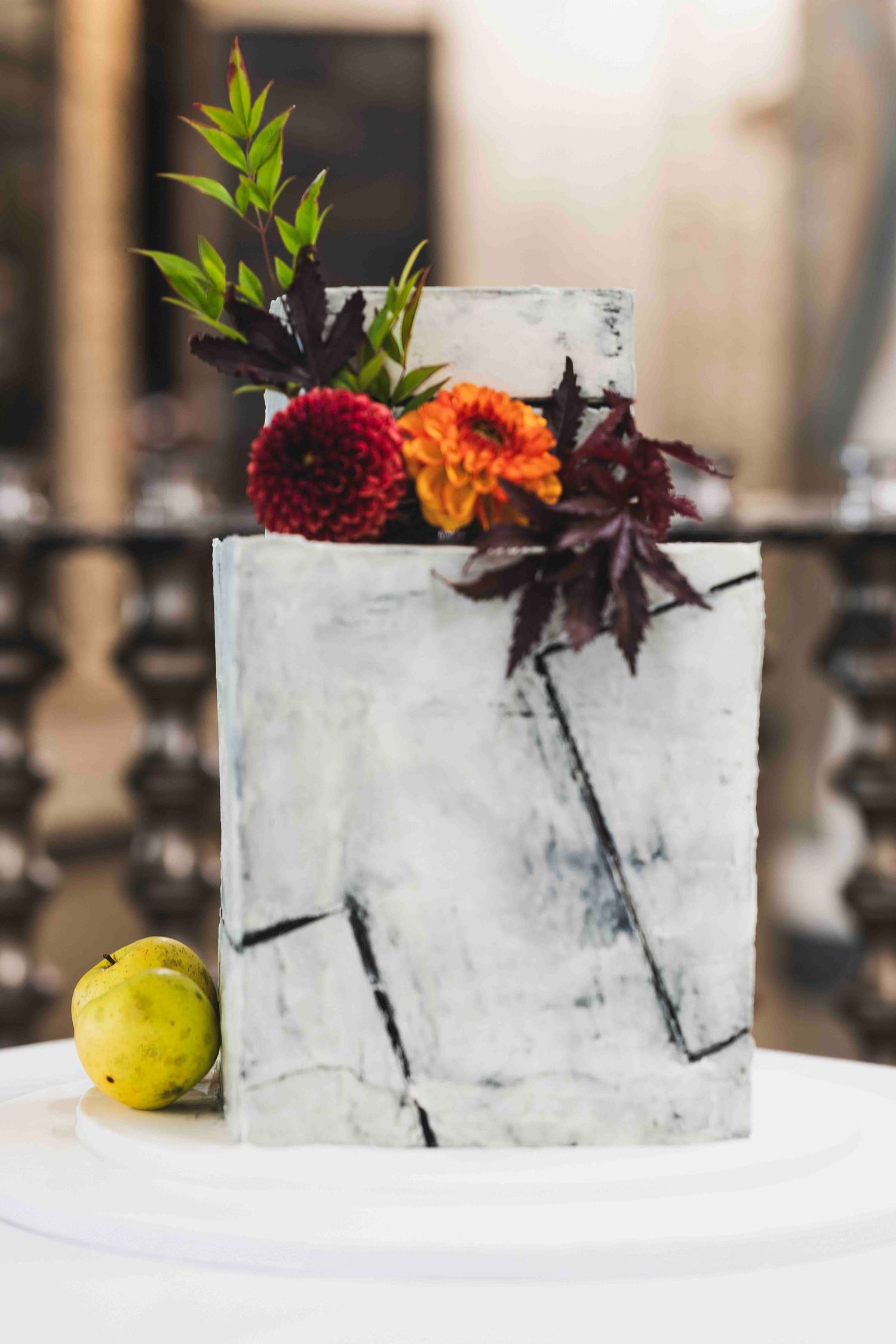 A white marbled wedding cake decorated with burgundy and orange flowers and dark foliage on a modern display.