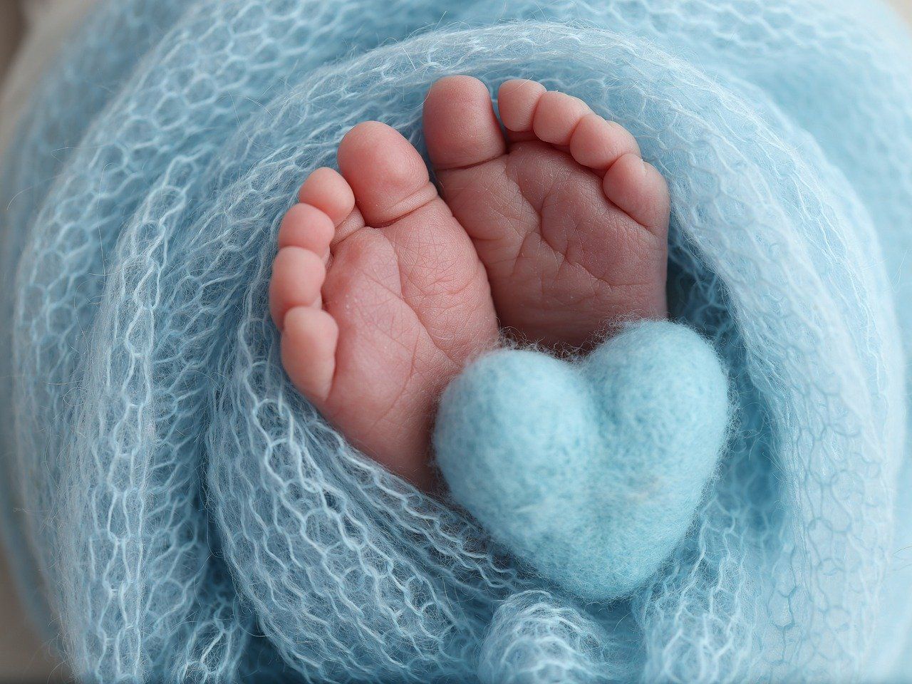 Close-up of a tiny baby hand grasping soft blue knit fabric.