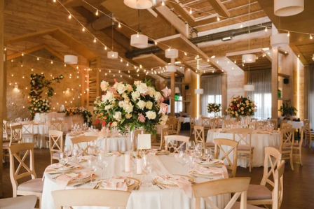 Elegant wedding reception venue with string lights, white floral centerpieces and round tables.