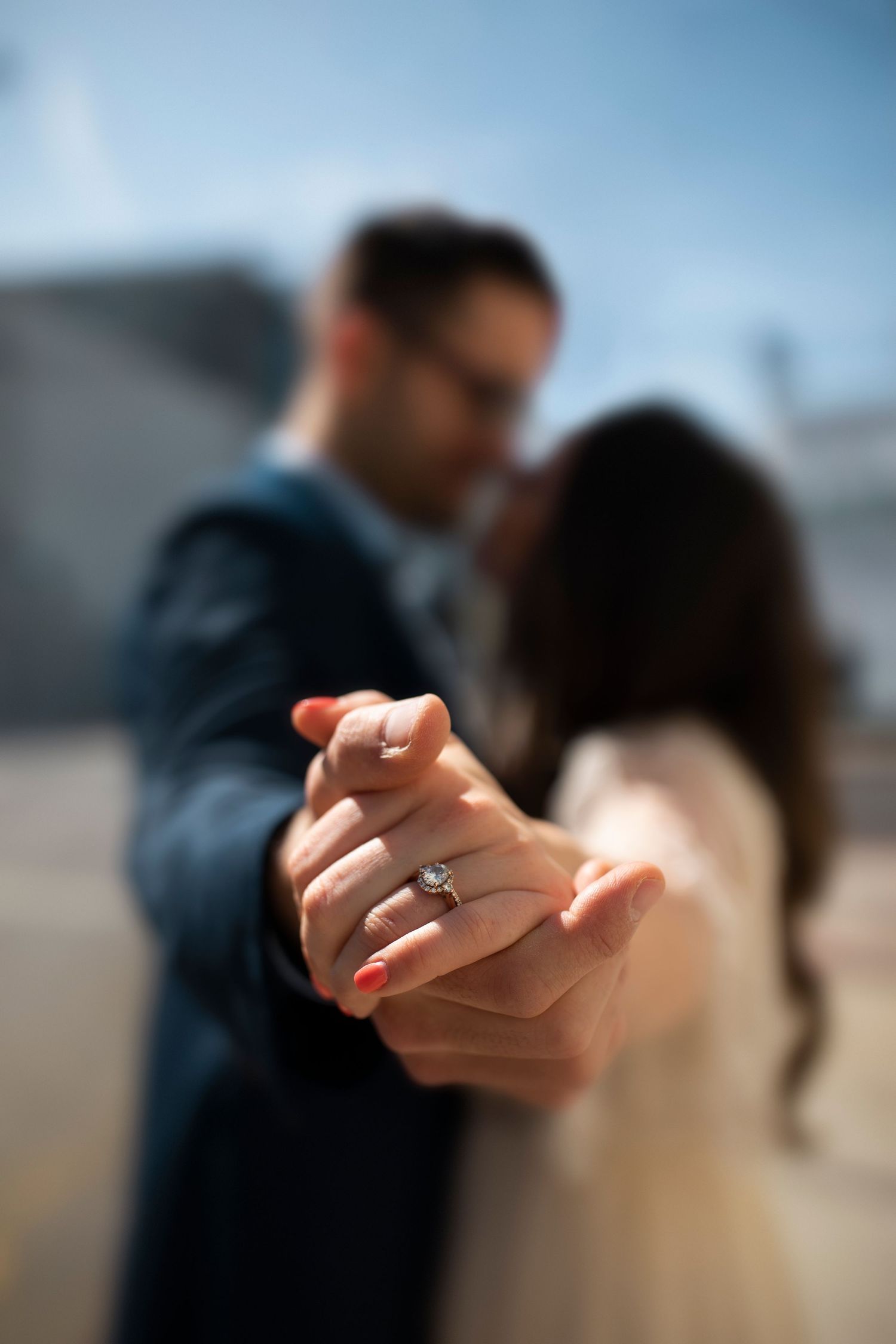 A close-up sequence showing an engagement ring on a hand with a beach and blurred couple in the background.