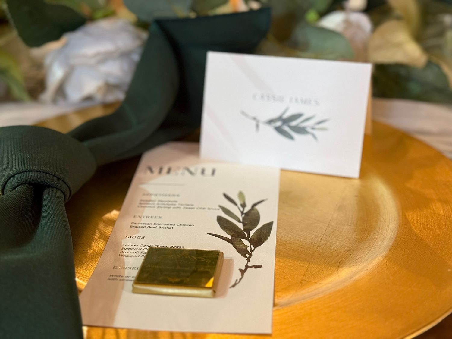 Elegant wedding menu cards with botanical designs and greenery details lay on a golden charger plate.