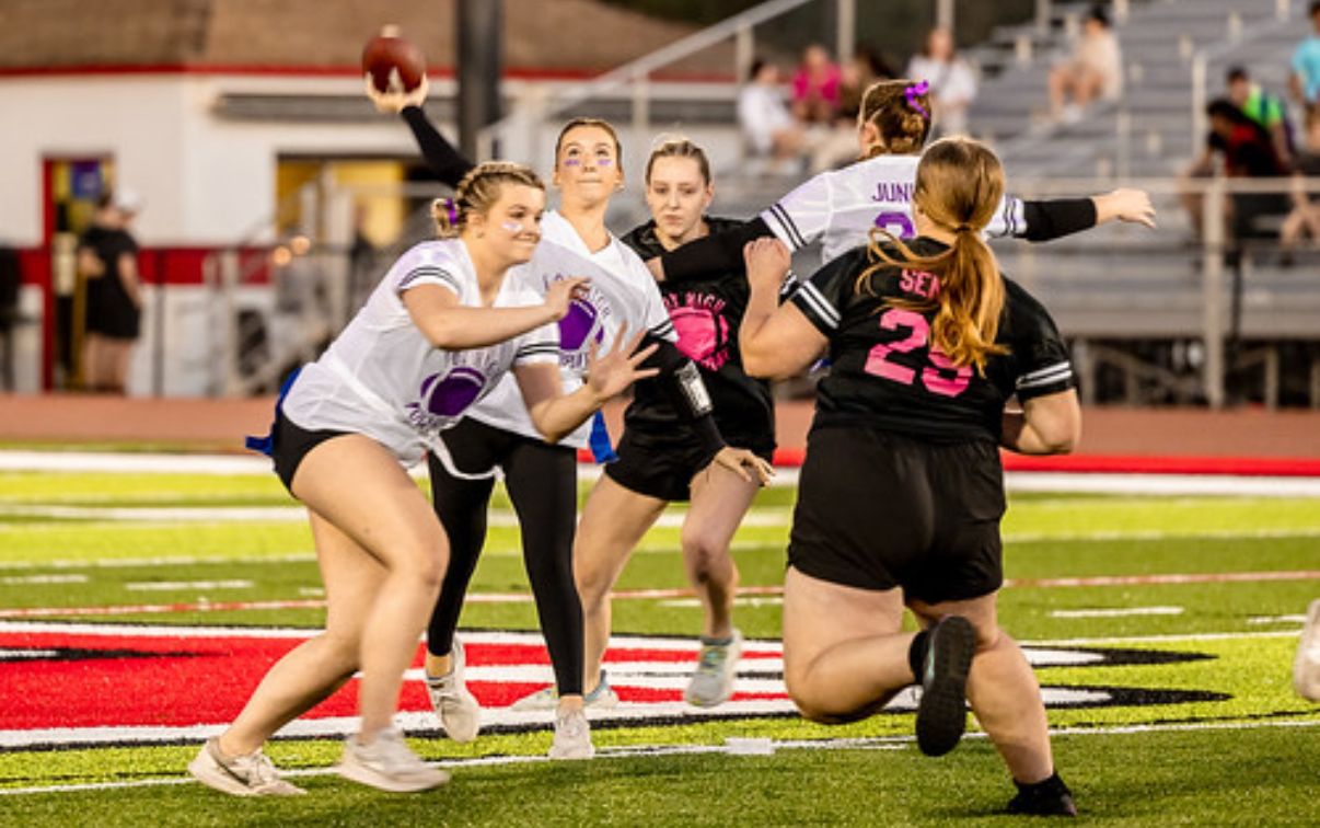 Flag football players compete on illuminated field during nighttime game with players dodging and defending.