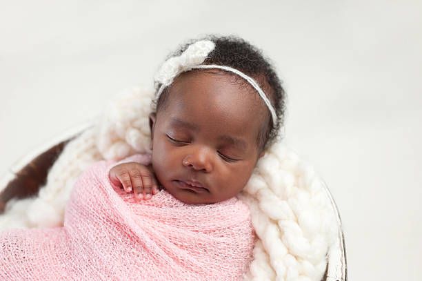 Sleeping newborn wrapped in soft pink blanket against white background.