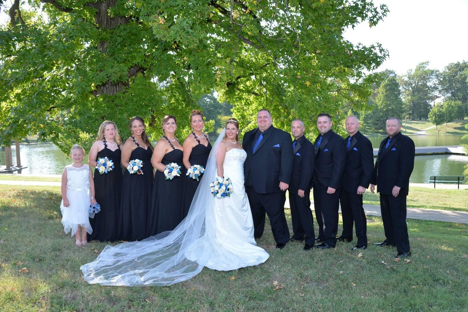 Wedding party poses together on lush green lawn during outdoor summer celebration.