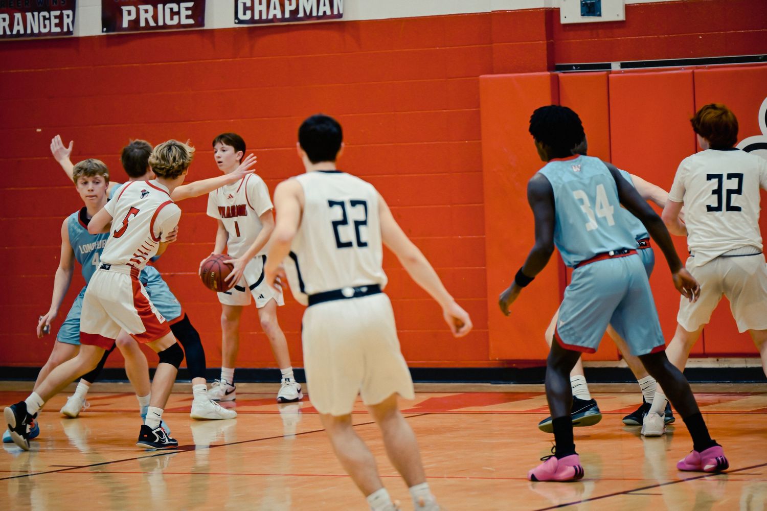 Basketball players compete for a loose ball on a bright orange court during an intense game.