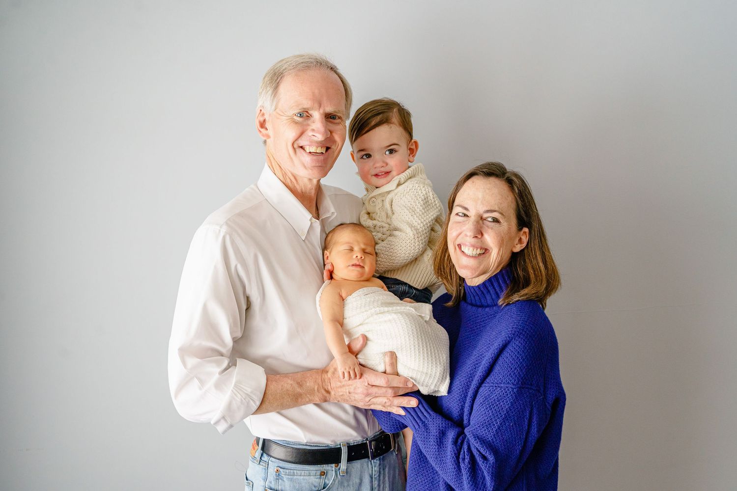 Family wearing coordinated blue and white outfits posing together against grey backdrop.