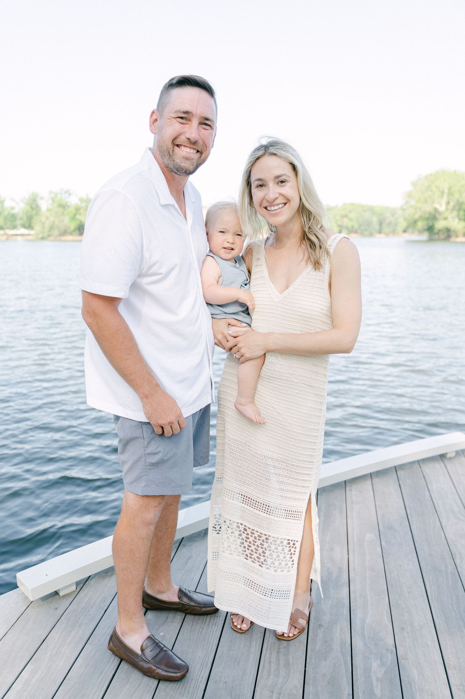 A family shares tender moments on a wooden dock by a serene lake on a bright summer day.