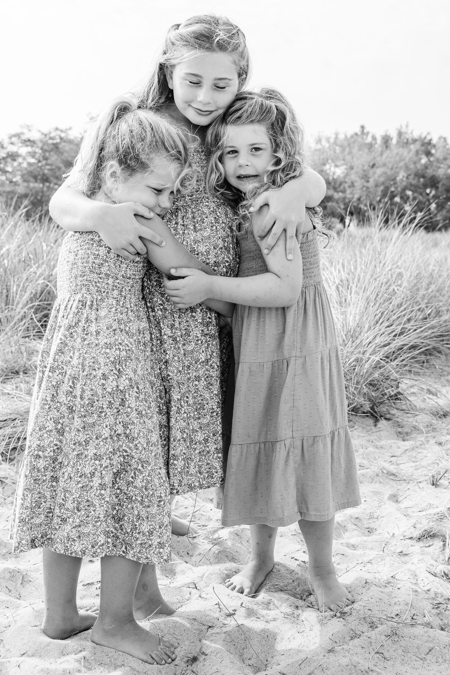 Two children in summer dresses share tender embraces while playing in a grassy field in black and white photography.