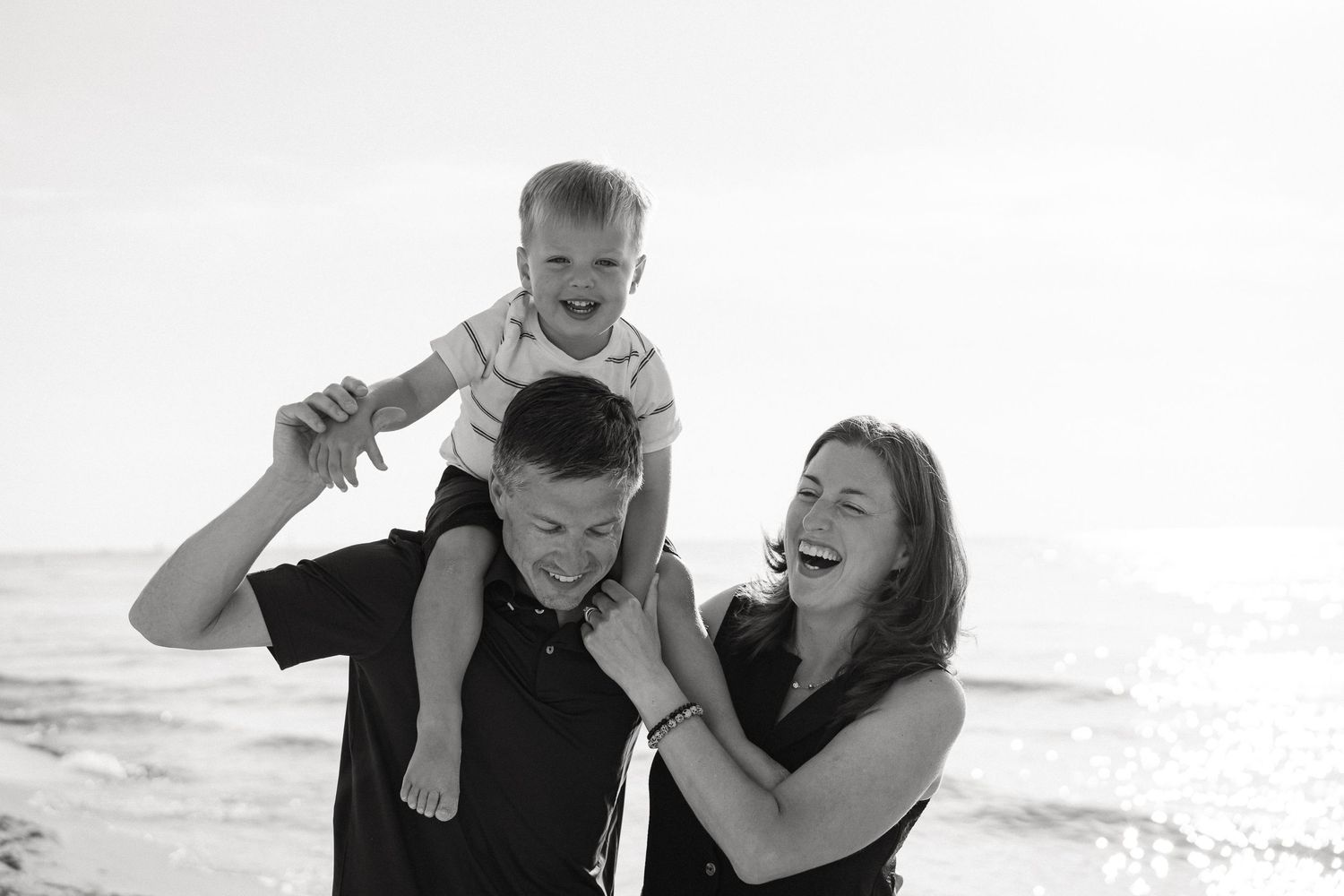 A happy family shares joyful moments together on a sunny beach in black and white photography.