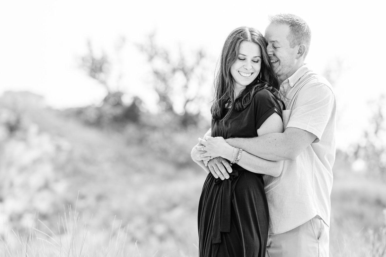 A romantic black and white portrait of a couple embracing outdoors.