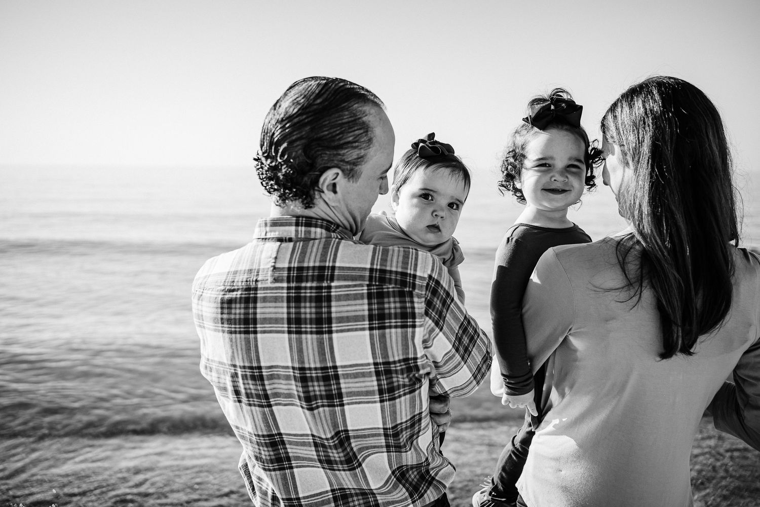 A series of black and white beach portraits showing intimate family moments along the shoreline at sunset.