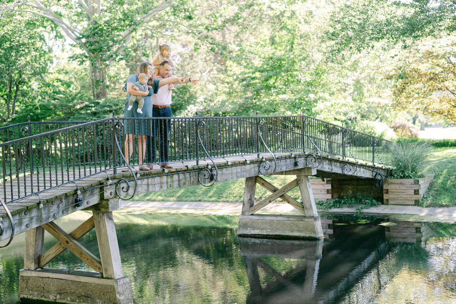 Scenic outdoor family portraits taken near a rustic wooden bridge over calm water.