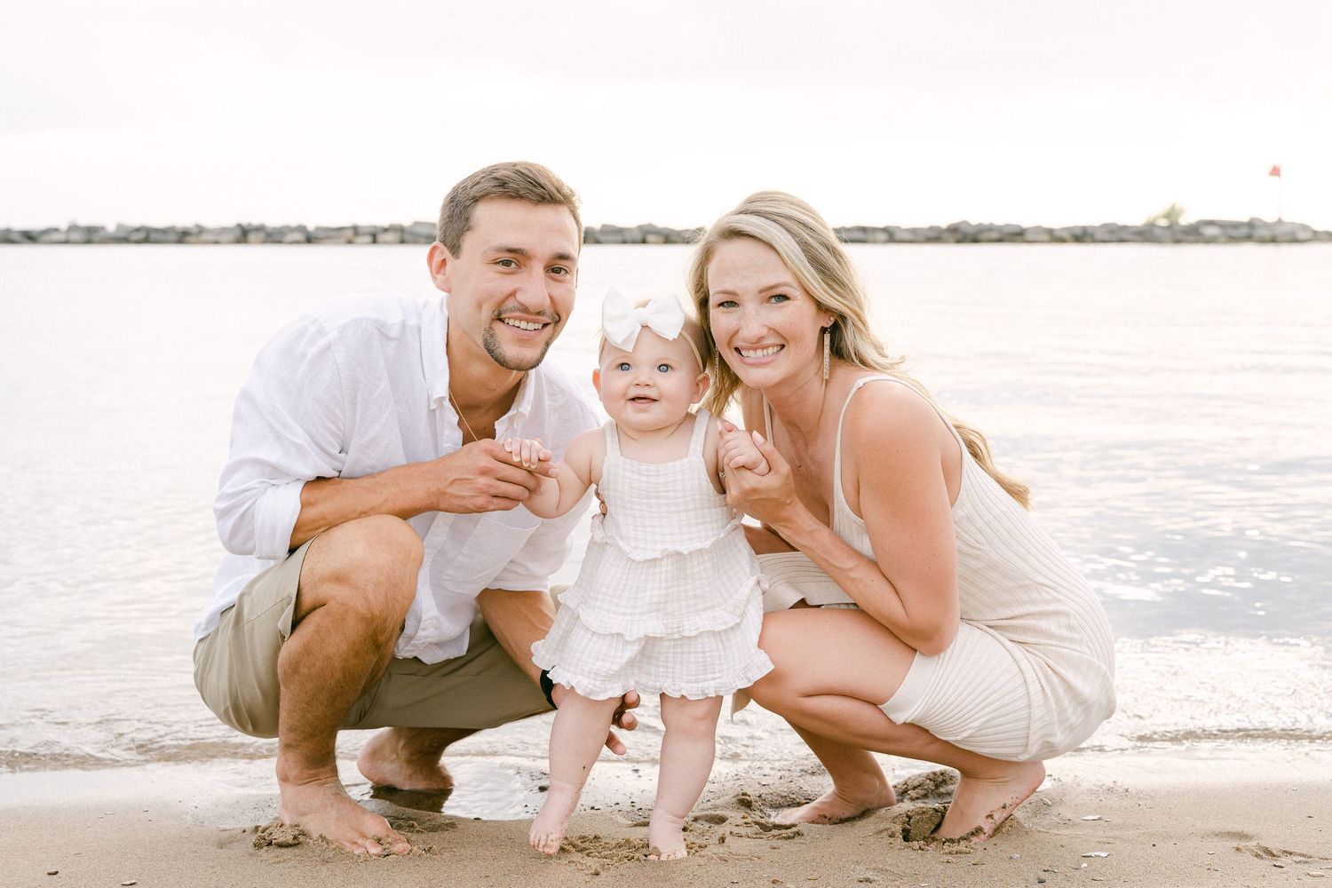 A family in light colored clothing plays together on a sandy beach at sunset.