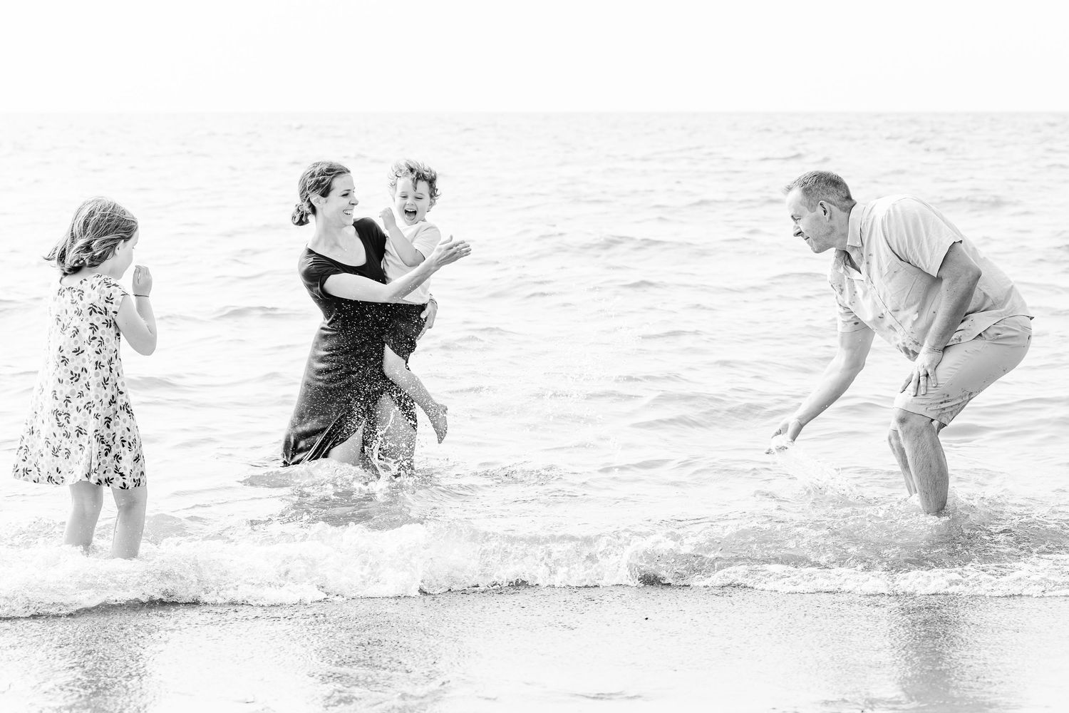 Children playing and splashing in ocean waves at the beach in black and white photography.