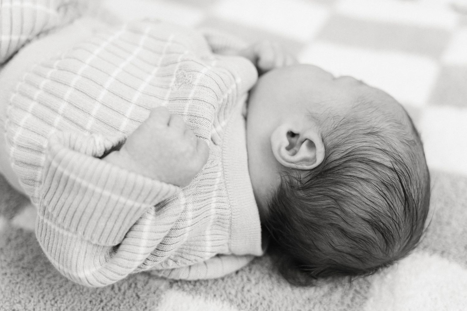 A series of black and white photos showing a sleeping newborn baby wrapped in a soft white blanket.
