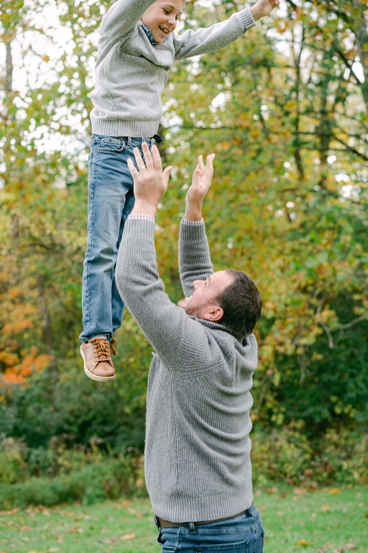 A playful moment captured as a parent lifts a child high in the air during an outdoor autumn photoshoot.