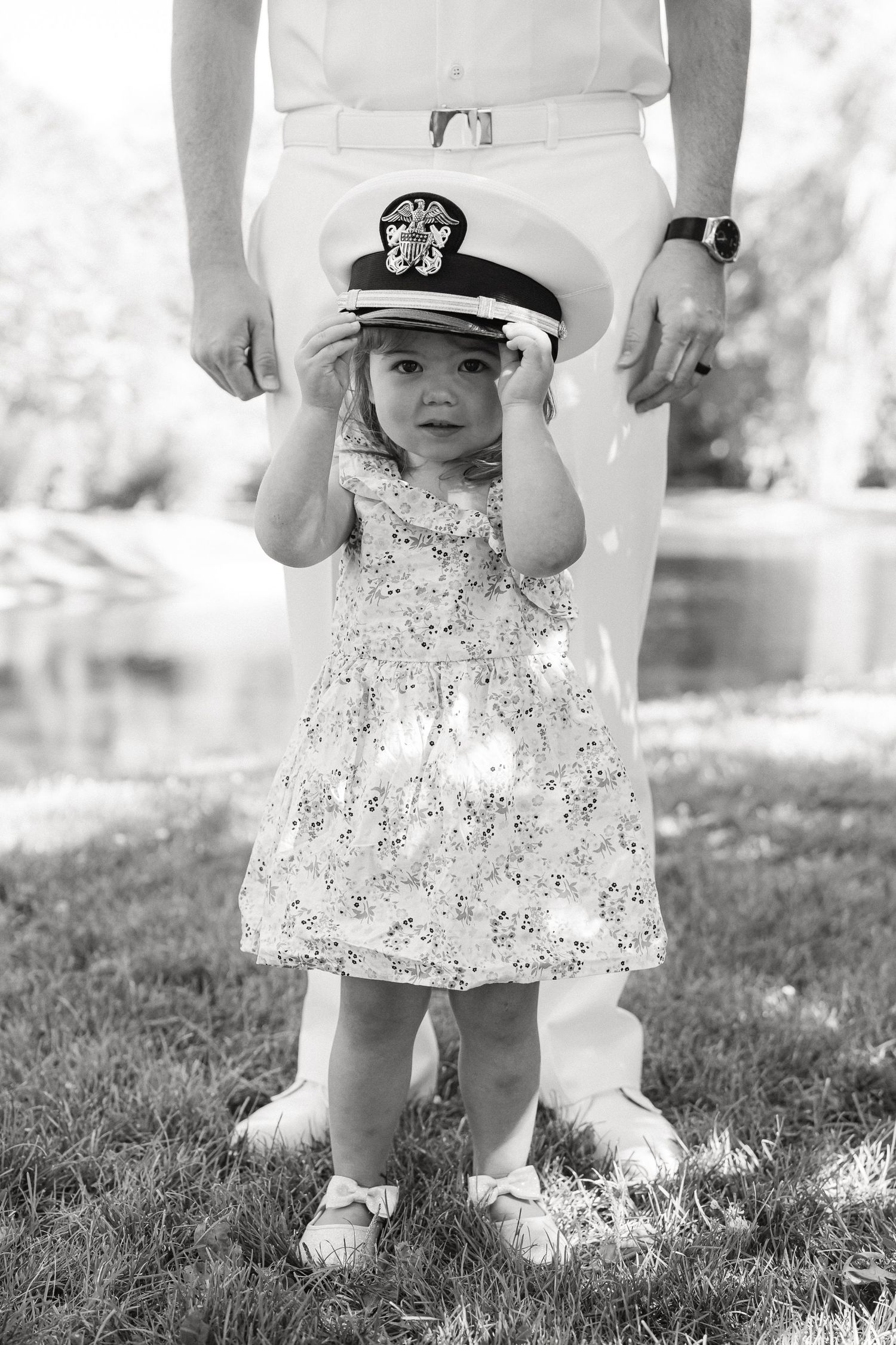 Black and white series of a small child in a floral dress and captain's hat standing on grass.