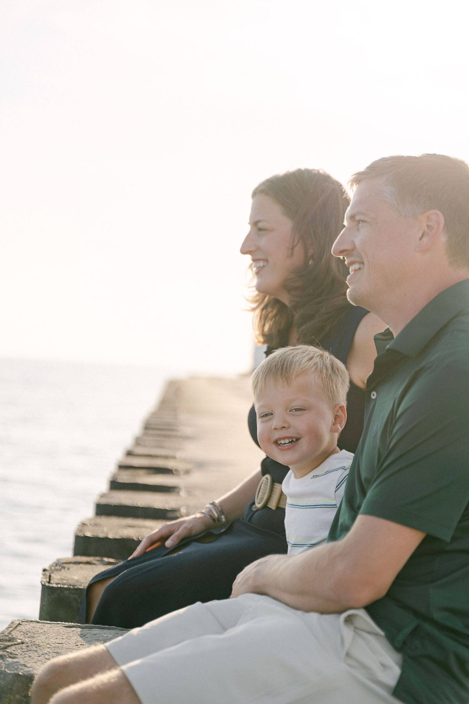 Family sits together on wooden pier at sunset enjoying peaceful ocean view.
