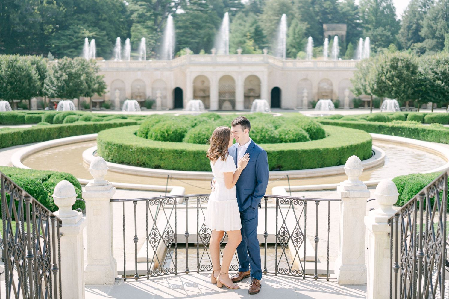 Romantic couple sharing tender moments in an elegant garden terrace with ornate stone railings and manicured hedges.