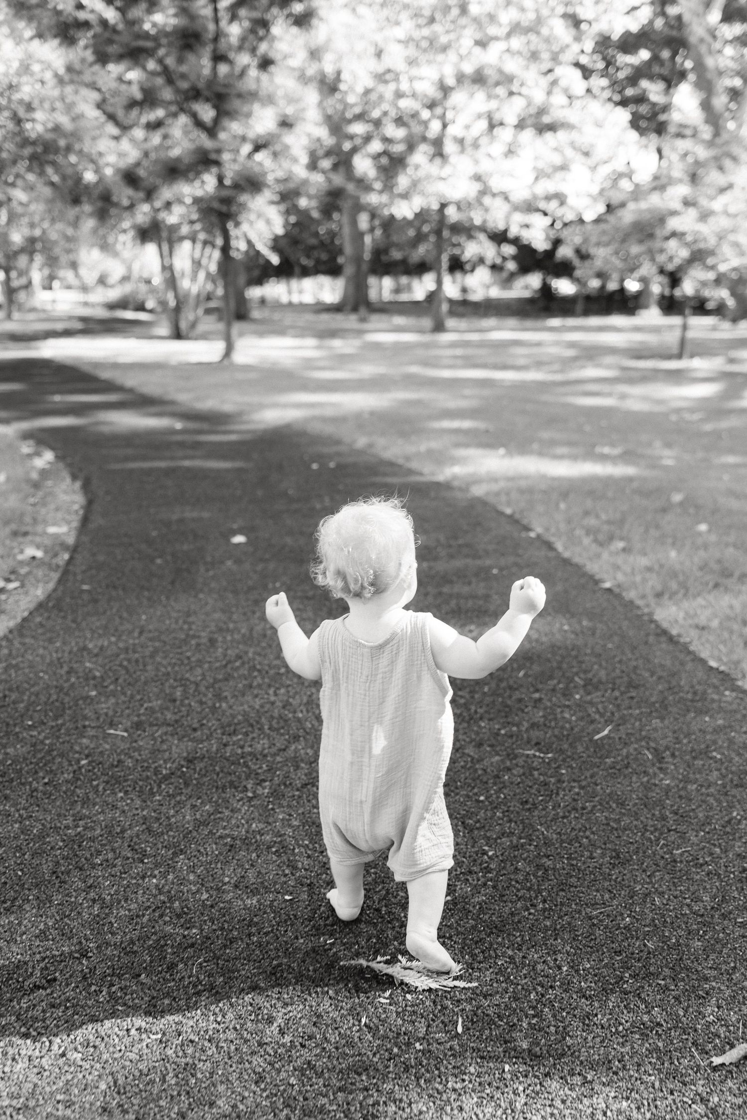 Black and white sequence showing a toddler in white clothing crawling on grass in a park.