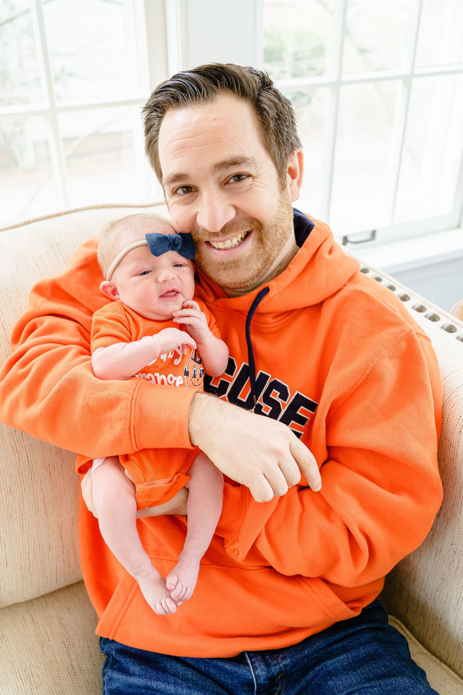 Playful family moments captured in bright orange sweatshirts by a sunlit window.