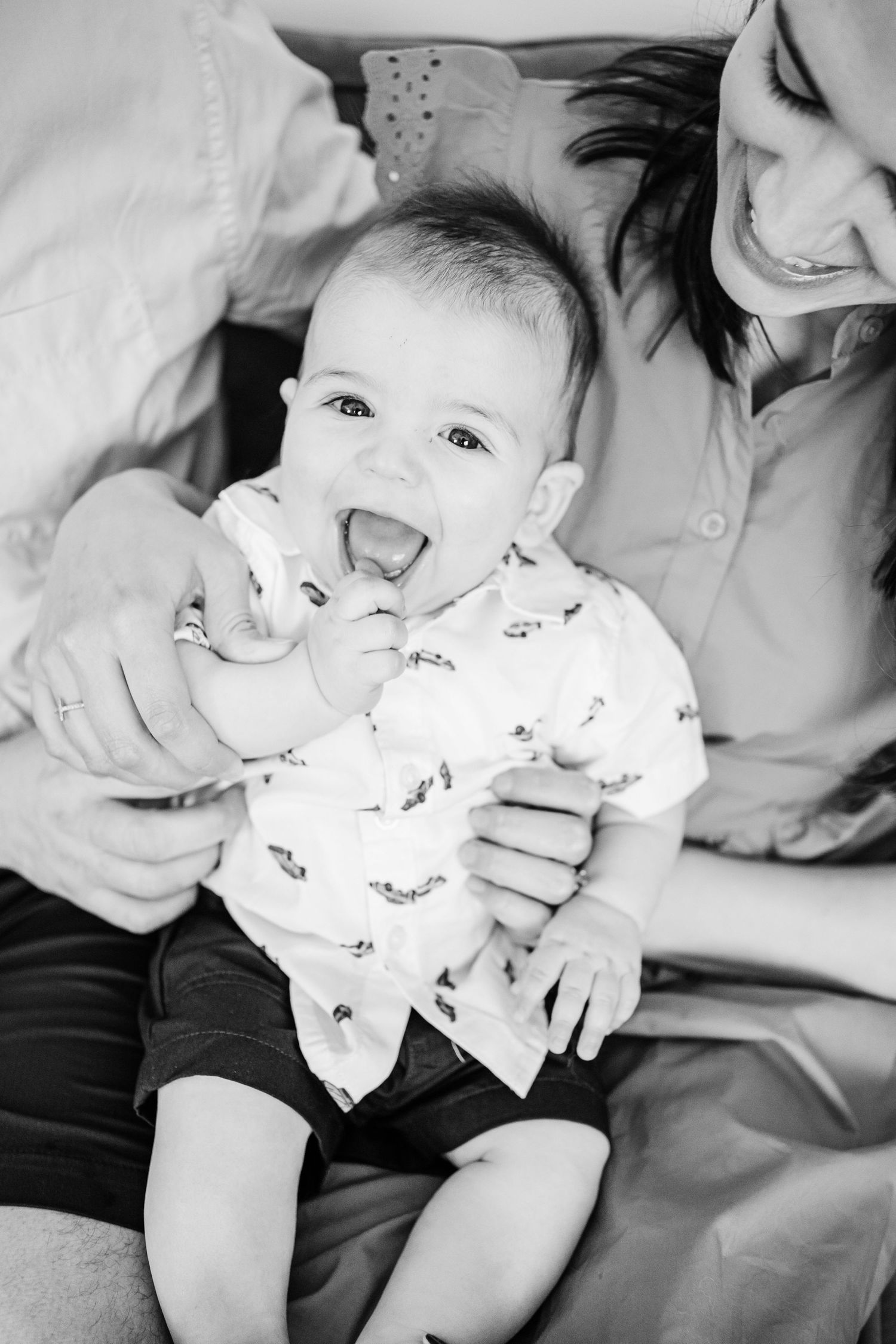 Black and white photo of a joyful baby in a patterned onesie laughing while being held.