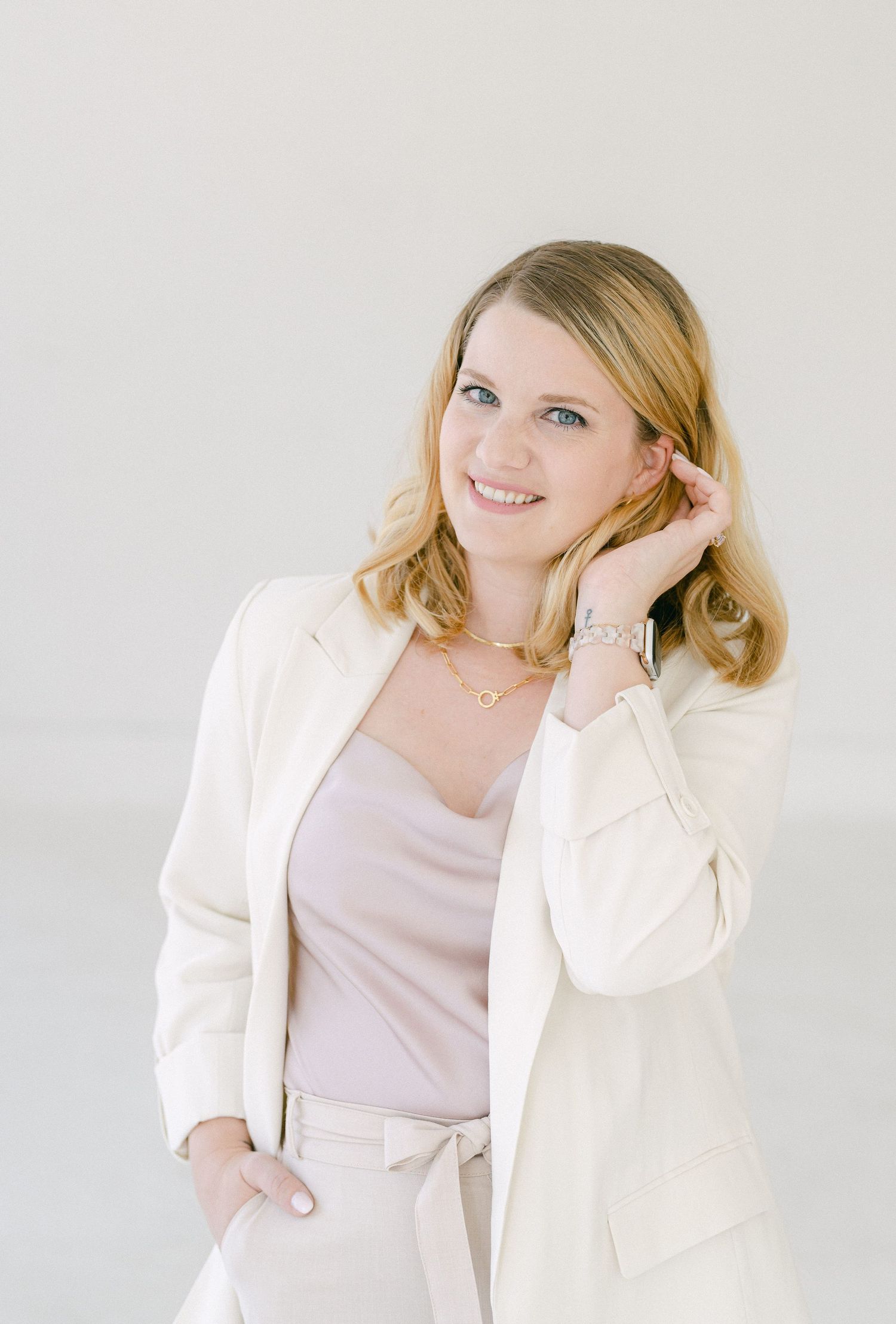 Professional portrait of someone wearing a cream blazer and pink top against a light neutral background.