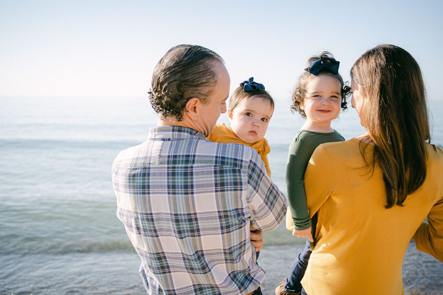 A family in coordinating plaid and yellow outfits shares tender moments together on a sunny beach.