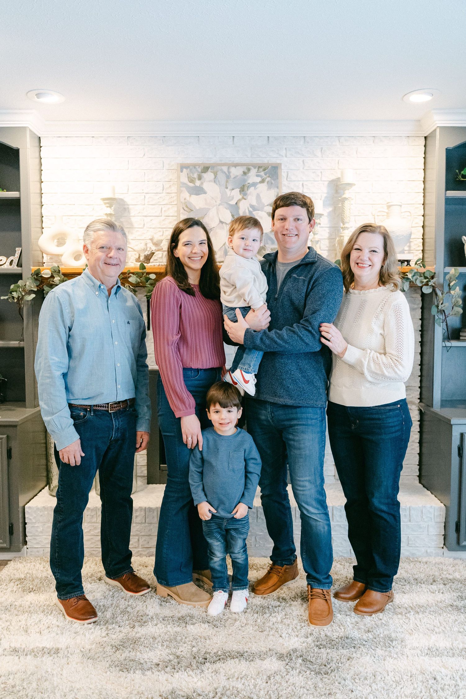 Family group wearing coordinated blue and white outfits poses together against white brick wall with holiday decor.