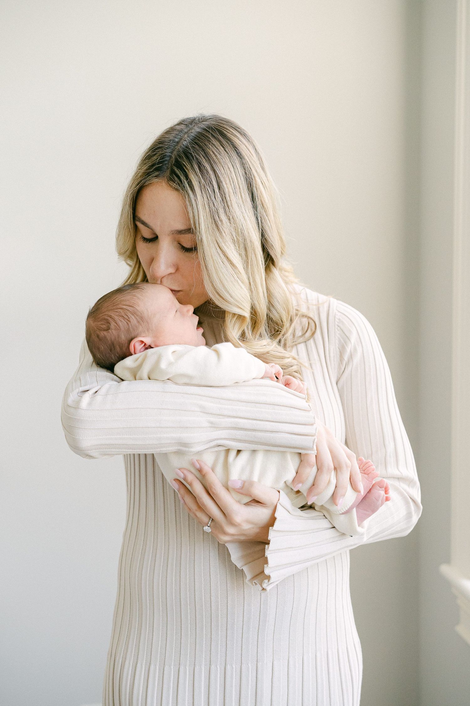 A series of tender moments showing a parent in white holding and kissing a newborn baby in soft natural light.