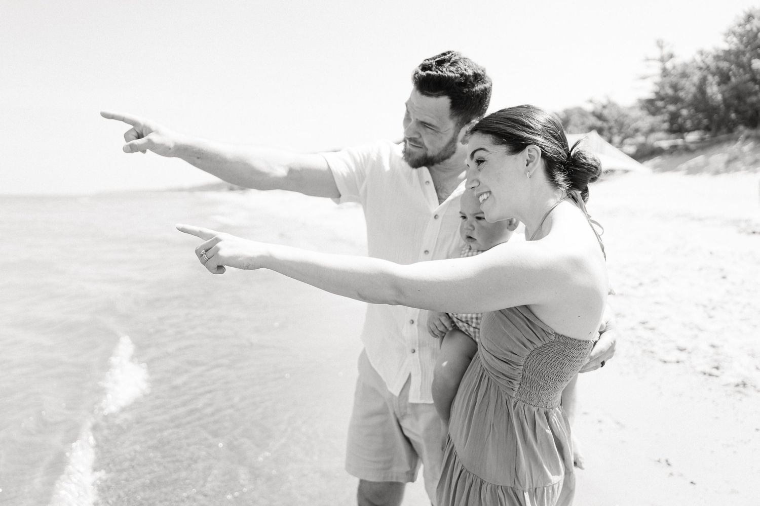 Two people playfully pose with outstretched arms on a sunny beach.