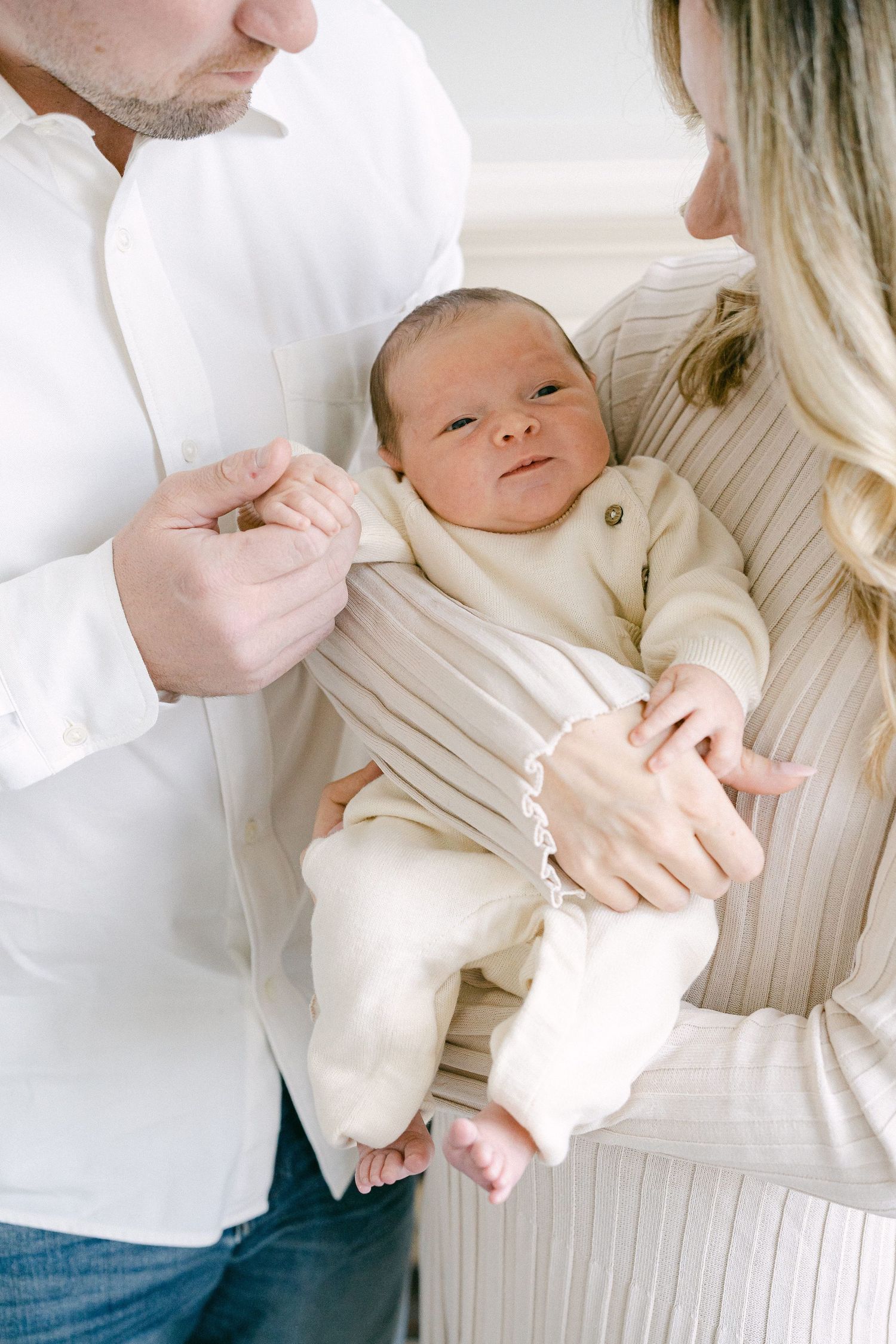 A collection of intimate photos showing a baby in white being cradled and held against a light background.