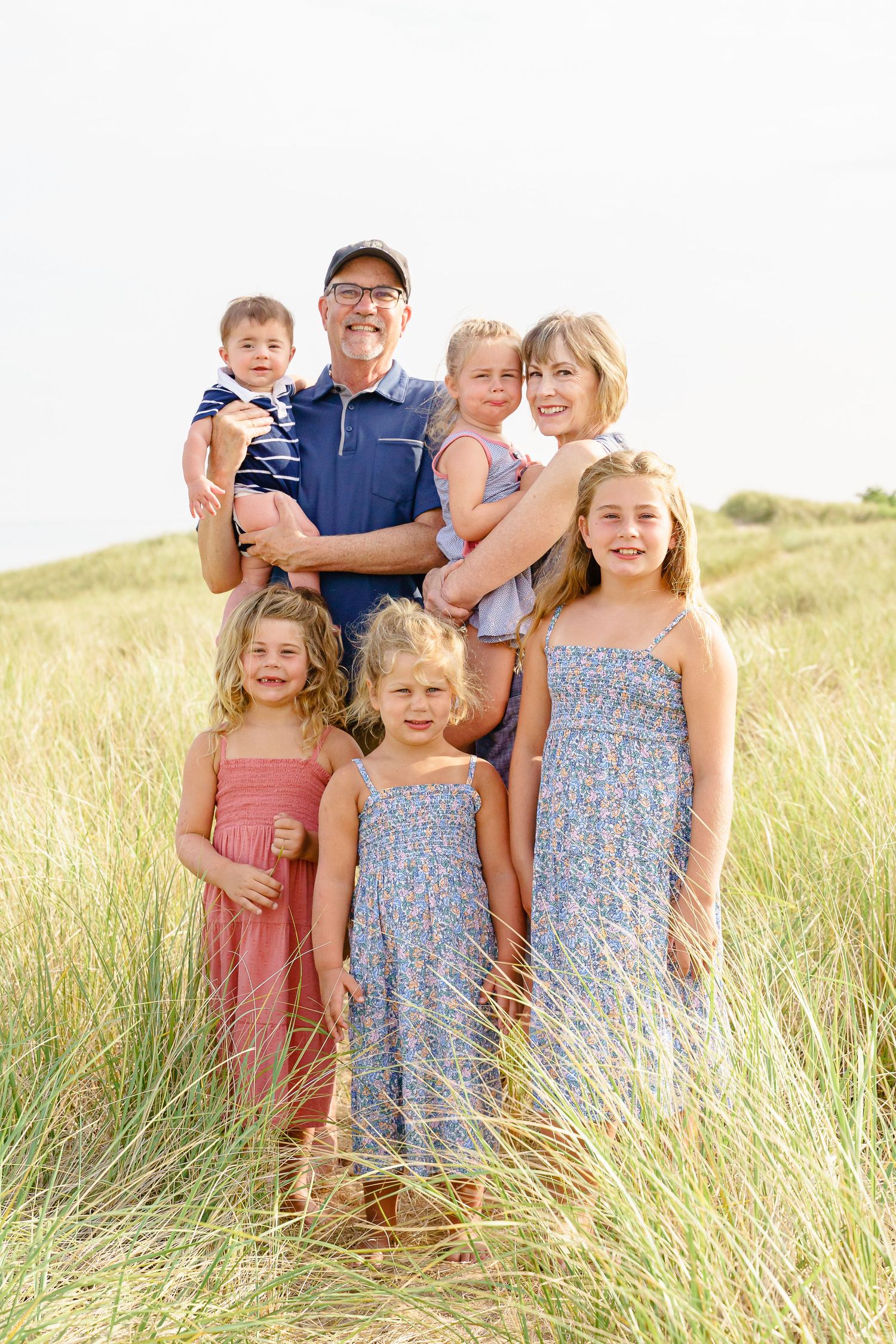 Family group stands together in tall golden grass during sunset outdoor portrait session.