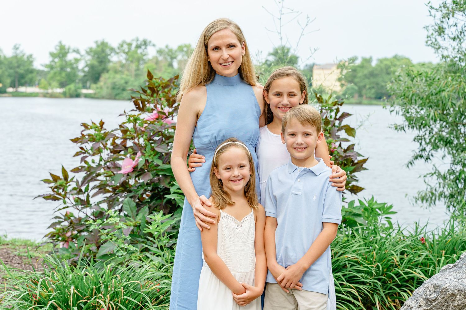 A family group poses together by a lake on a sunny day wearing coordinated blue and white outfits.