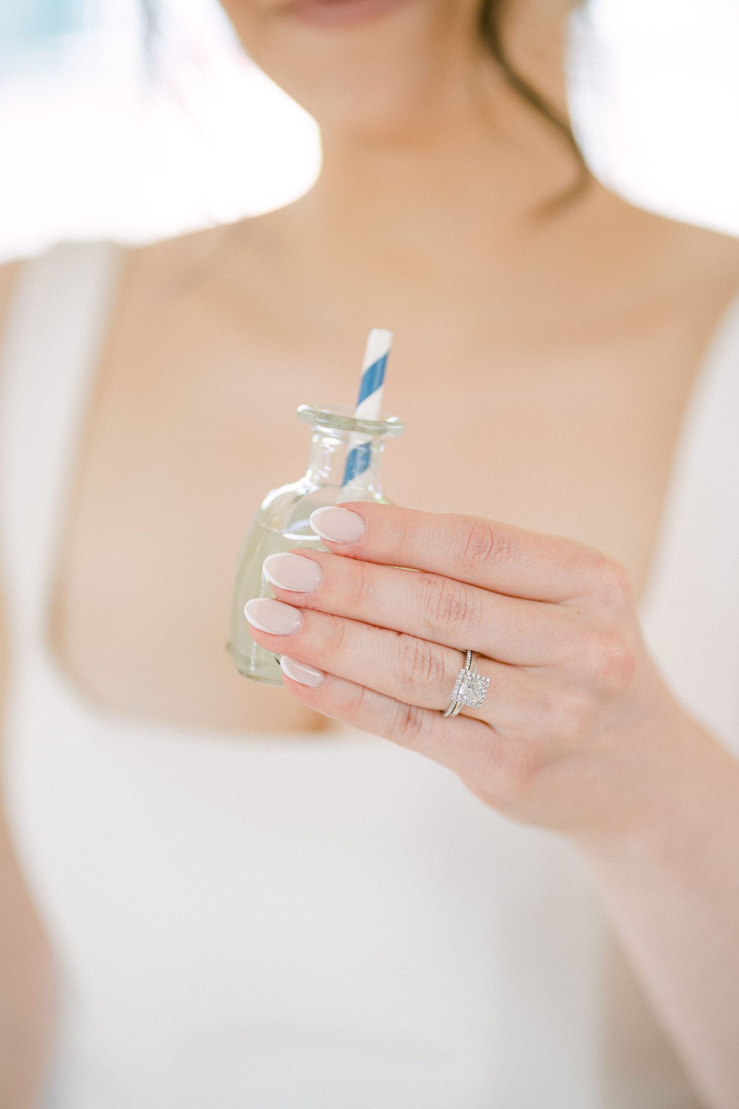 Bride holding a small glass bottle with a blue striped straw, showcasing a diamond engagement ring and pink manicure  in Miami, FL