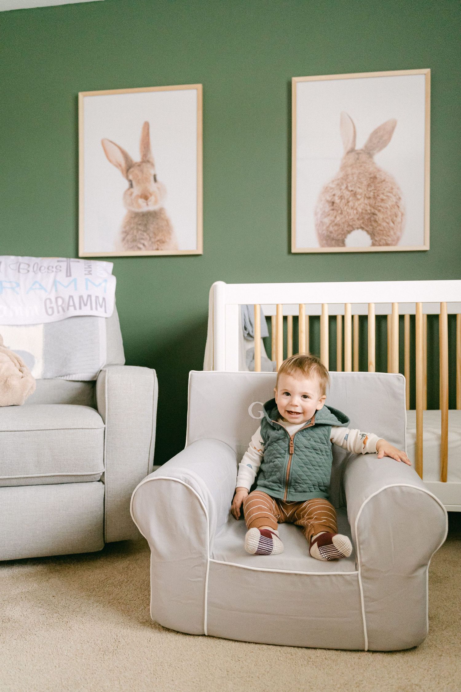 A nursery room with green walls features bunny artwork and a cozy grey chair against a minimalist design.