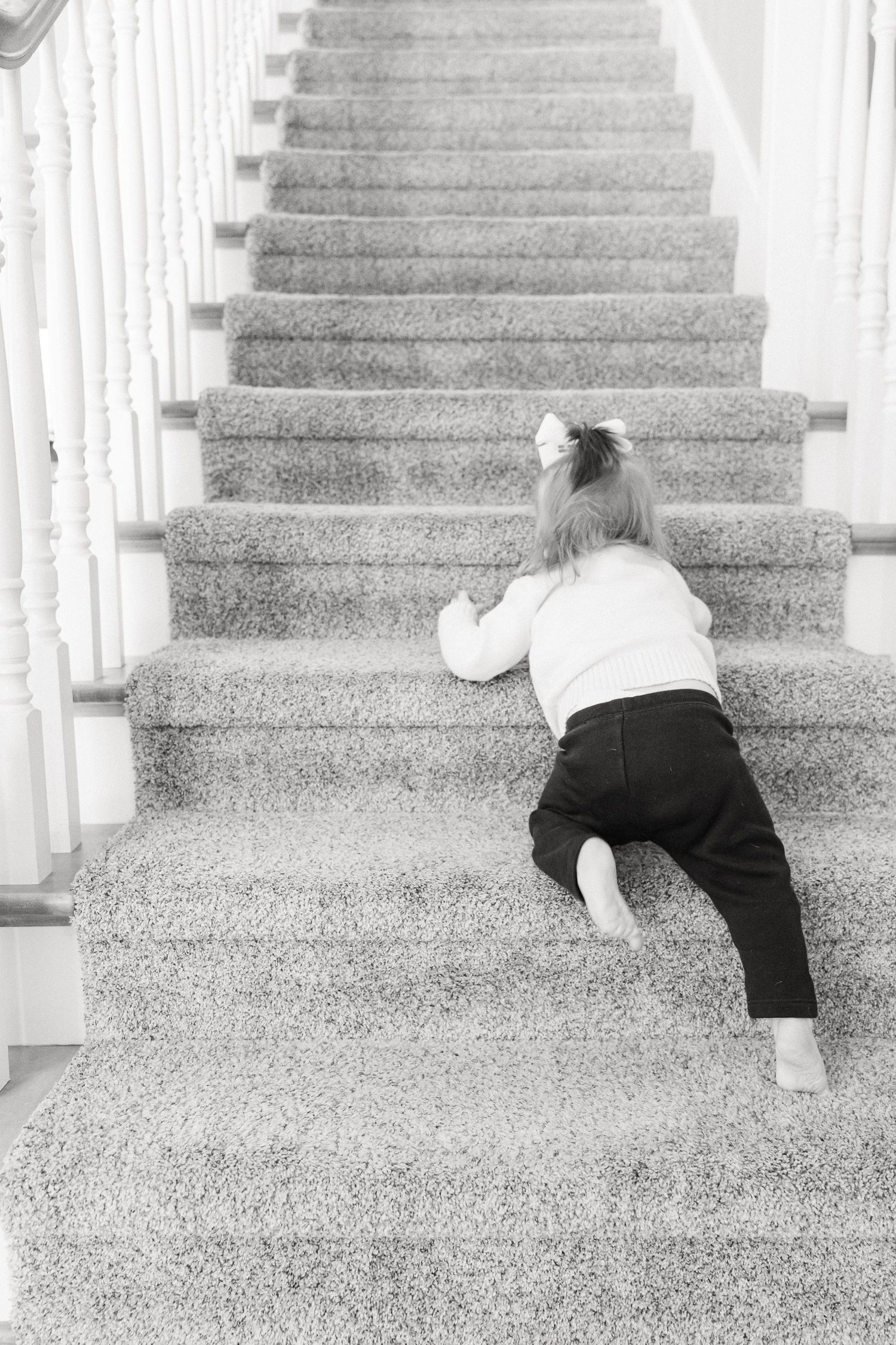Sequence of a small child crawling up carpeted stairs in black and white photography.