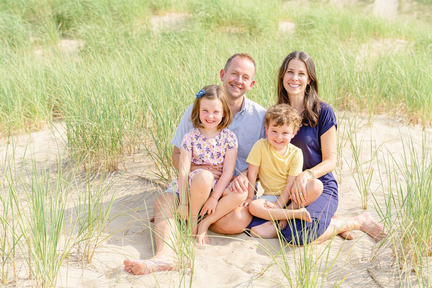 A family enjoys a sunny day together on grassy sand dunes at the beach.