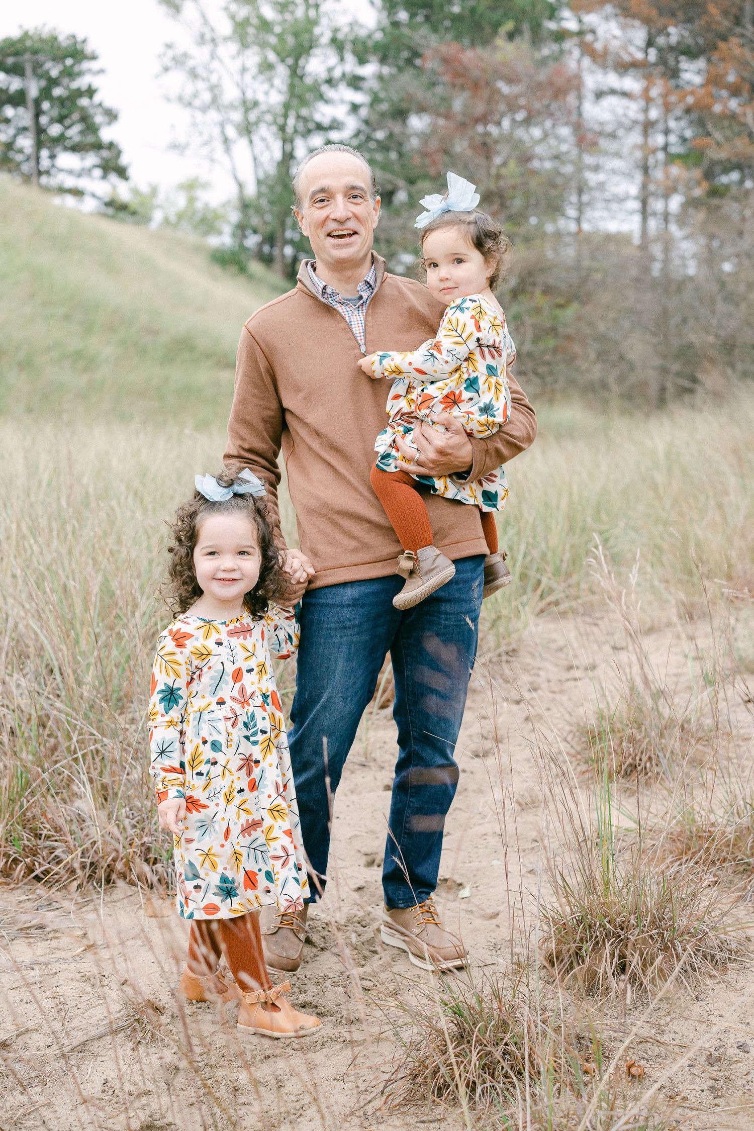 Family enjoying a playful moment together on sandy dunes surrounded by tall grass on an autumn day.