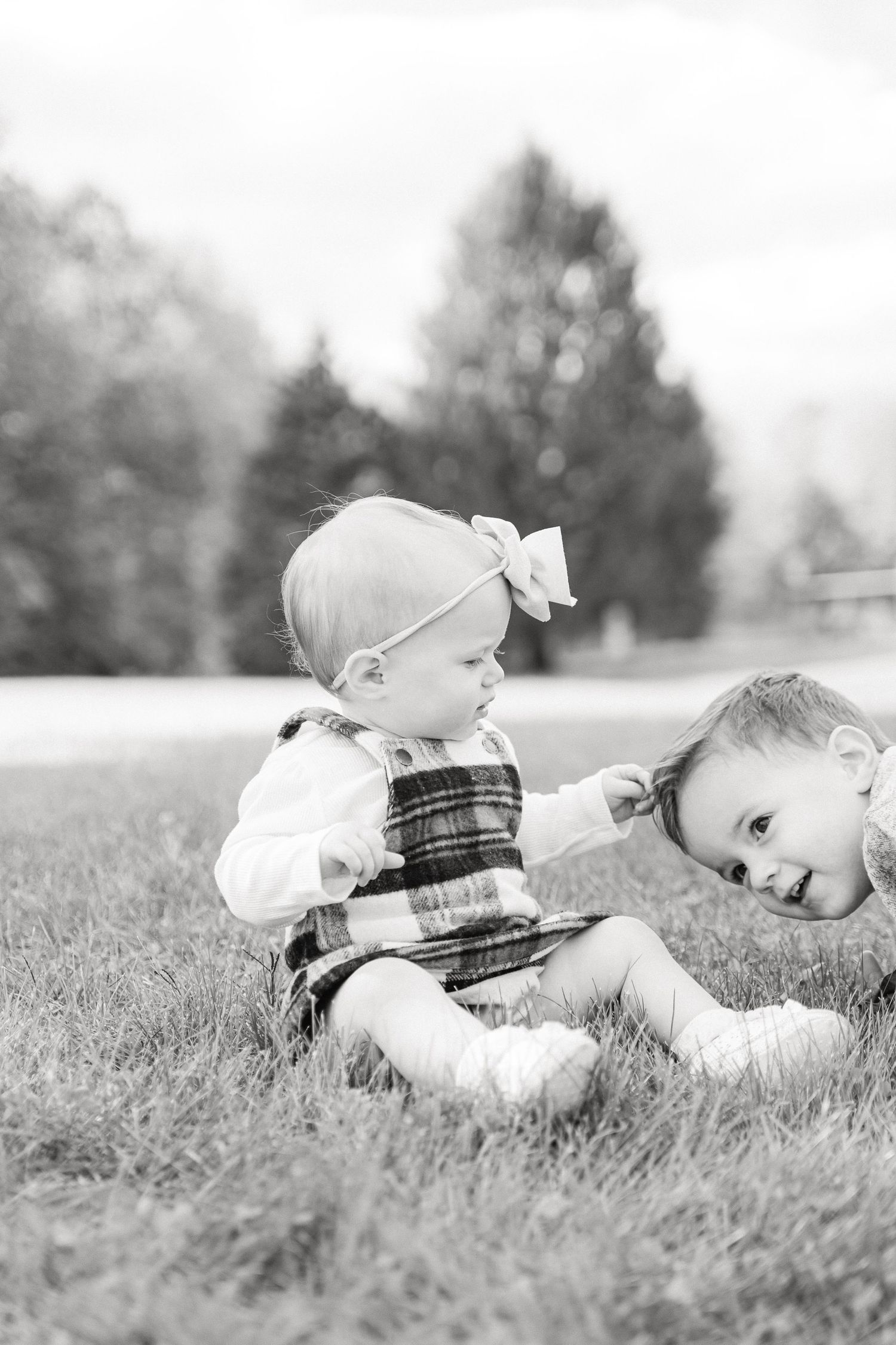 A black and white series of photos showing a baby in plaid clothing lying in grass and rolling over.