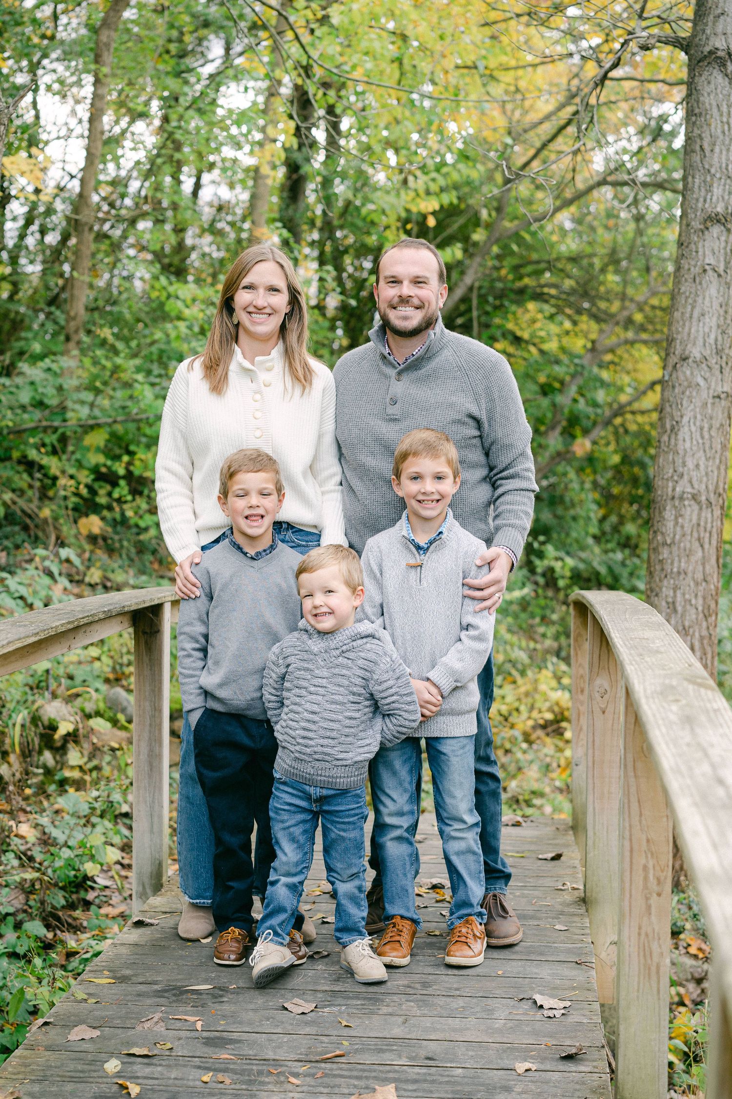 A group wearing coordinated grey and navy outfits poses together on a wooden walkway surrounded by autumn foliage.